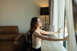 © Parichat - Woman opening curtains embracing new day sunlight