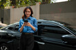 © Parichat - Woman using phone near car connecting to technology