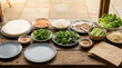 © Video80X - Vietnamese spring roll ingredient spread with rice paper sheets, shrimp, rice noodles, sliced pork, lettuce, cucumber sticks, fresh herbs, bean sprouts, dipping sauce, and empty plates on wooden table