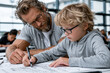 © Juan - teacher assisting young boy with writing and drawing task
