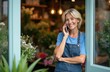 © miss irine - Smiling woman owner talks on phone in bright flower shop. Female florist takes floral orders and arranges bouquets with care. Small business person works happily preparing orders.