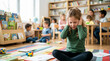 © Xenia - Stressed young girl covering ears while sitting on classroom floor. Student experiencing sensory overload during class