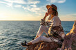 © svetograph - Woman sunset ocean traveller sits on rocky cliff enjoying peaceful golden hour view with copy space