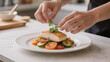 © Alodie - Hands adding herbs to seafood dish.
