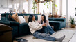 © DMegias - Two women relaxing on the floor, talking and bonding, with a cat and plants in a cozy bright living room