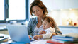 © akridiy - Mother studying on laptop with sleeping baby at kitchen table