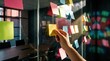 © snd studio - Hand placing a colorful sticky note on a glass wall filled with ideas, representing an office brainstorming session and collaborative strategic planning
