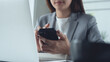 © tippapatt - Close up of business woman using smartphone during working on laptop computer at office.