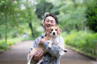© kapinon - 新緑背景で愛犬のビーグルを抱く男性の笑顔、公園で過ごす幸せなお散歩時間のカメラ目線クローズアップ