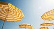 © SHALENA - Low angle view of yellow and white striped beach umbrellas against blue sky