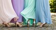 © Tatiana - Women in colorful long evening dresses standing on stone pavement. Elegant bridesmaids in pastel gowns wearing high heel shoes. Celebration, wedding fashion and friendship concept.