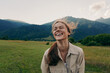 © SHOTPRIME STUDIO - Happy woman enjoying outdoor life, smiling in a grassy field with mountains in the background, casual jacket, sunlit moment, lifestyle portrait of carefree everyday joy