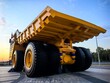 © Алина Неборская - Low angle view of a giant yellow mining dump truck with massive tires, blue metal stairs and safety railings against dramatic cloudy blue sky. Heavy industrial mining vehicle concept.