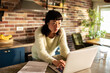 © Davor - Focused woman paying bills on laptop in home kitchen