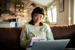 © Davor - Woman taking notes while working on laptop in cozy living room