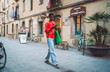 © BullRun - Young woman using smartphone walking city street, mobile application, 5G internet, digital lifestyle, orange sweater, green bag, remote work, communication, authentic representation, innovation.
