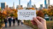 © Salim - A hand holding a white paper note with an inspirational quote in a blurred autumn city park