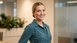 © Vasiliy - Portrait of a smiling young businesswoman in a modern office. Confident female professional wearing a teal shirt standing in a corporate workspace
