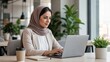 © Olga - Young Arab woman working on laptop in modern office with plants