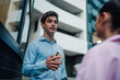 © Zamrznuti tonovi - Young businessman having a conversation with a colleague outdoors, holding smartphone in modern urban setting