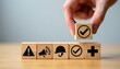 © Pete - Wooden cubes show work safety icons. A hand places a checked cube, signifying compliance and positive outcome. Concepts include hazard alert, communication, protection, and health.