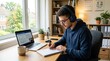 © Coosh448 - Young man studying at a desk with headphones in a bright room, focused education and remote learning lifestyle scene, student productivity, concentration and technology concept, notebook and laptop