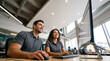 © Milan - Smiling business colleagues working together on a computer in a modern office. Happy man and woman in matching grey polo shirts looking at a monitor at their desk. Corporate teamwork concept