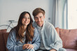 © Daniel - Smiling young couple sit close on a cozy couch in a bright living room, sharing a relaxed moment together that conveys warmth, intimacy, friendship and modern home lifestyle.