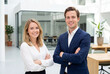 © Meow Creations - Confident business man and woman colleagues with arms crossed smiling in a modern office lobby