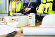 © Nuttapong punna - Engineer team in safety helmets discussing house model and blueprint. Construction planning, architecture design, project management