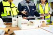 © Nuttapong punna - Engineer team in safety helmets discussing house model and blueprint. Construction planning, architecture design, project management