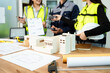 © Nuttapong punna - Engineer team in safety helmets discussing house model and blueprint. Construction planning, architecture design, project management