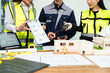 © Nuttapong punna - Engineer team in safety helmets discussing house model and blueprint. Construction planning, architecture design, project management