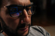 © dikushin - Close-up portrait of bearded trader focusing on financial data and stock market trends, trading cryptocurrency and investments online, with screen reflections visible in blue light blocking glasses.
