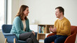 © OlgaNeuroArt - Female therapist talking with a young man with Down syndrome. Counseling session and communication support for a person with special needs. Mental health and inclusion concept