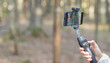 © valiantsin - Smartphone on a handheld gimbal in a forest. Mobile video recording setup for outdoor content creation. Nature background with travel and vlogging technology..