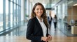 © Masque - A confident businesswoman smiling while standing in a modern office hallway.