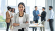 © SolaruS - Confident female professional in a grey blazer stands in a bright office. Her diverse team works behind her, symbolizing leadership, success, and collaboration in a modern corporate setting.