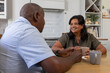 © Wavebreak Media - Mature African American couple holding mugs, sitting at wood table in kitchen with plate of cookies