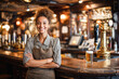 © Kowit - A smiling bartender stands confidently behind the bar in a cozy pub with wooden decor and a draft beer on the counter.