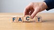 © muhammadhasnain - Hand arranging wooden blocks spelling fact on a table with a plain background