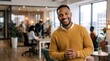 © Vasiliy - Smiling Black man in a yellow sweater standing in a modern office. Confident creative professional in a casual corporate workplace. Teamwork concept