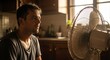 © SashaMagic - Sweaty man cools down in kitchen with fan during golden hour heatwave, seeking relief from summer heat