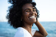 © SISMIZ - Joyful Black woman with curly hair smiling brightly by the ocean
