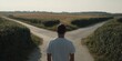 © Rifqi - Young man facing a fork in the road in a rural setting, concept for making hard decisions, career path uncertainty and life choices guidance