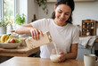 © Meow Creations - Smiling young woman pouring plant based milk into a glass