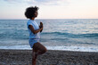 © SISMIZ - Woman practicing yoga tree pose on a pebble beach at sunrise