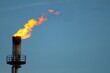 © Koapan - Industrial gas flare stack burning with bright orange flame against blue sky at petroleum refinery or chemical plant illustrating energy production and fossil fuel emissions. Copy space.