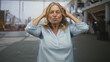 © Krakenimages.com - Senior woman with blonde hair wearing light blue blouse touches cheek with hand, closes eyes and tilts head back in airport terminal building; calm relief.