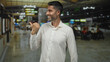 © Krakenimages.com - Man smiling with thumbs up pointing left in airport terminal, wearing white shirt and visible beard; confidence travel ease.